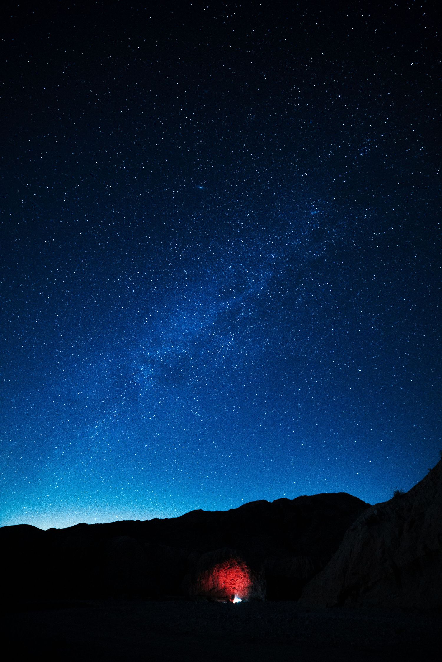 Starry night sky over mountain silhouette with red glow at base.