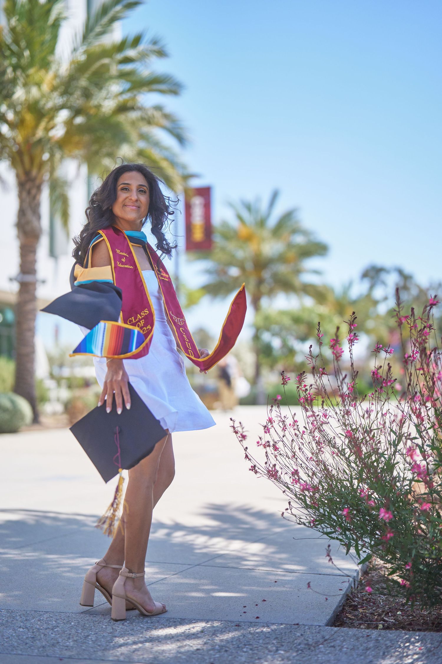 Graduate celebrating with colorful stoles and graduation cap against palm trees.