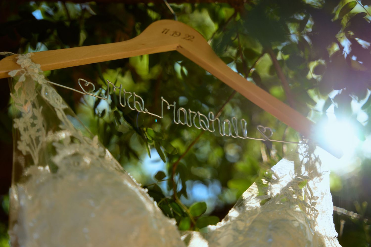 Custom wire name wedding dress hanger reading Sandra Marshall hanging outdoors among green leaves.