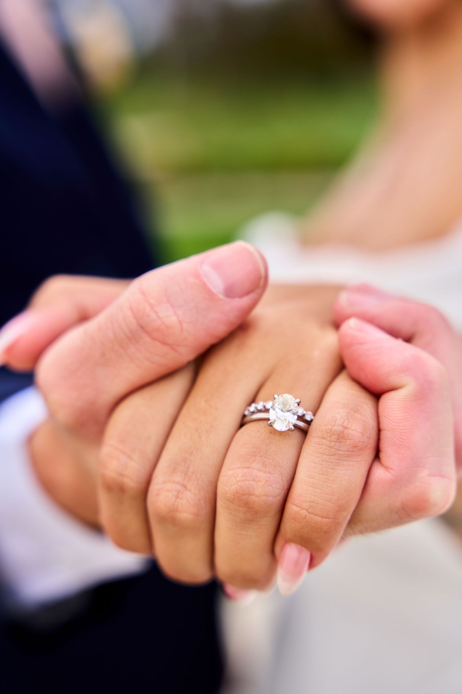 Close-up of a couple holding hands displaying a stunning diamond solitaire engagement ring on the bride's finger.