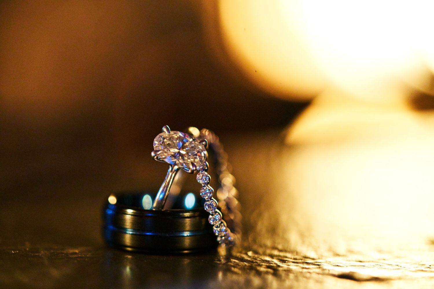 Diamond engagement ring with wedding bands displayed on golden bokeh background, elegant jewelry photography.