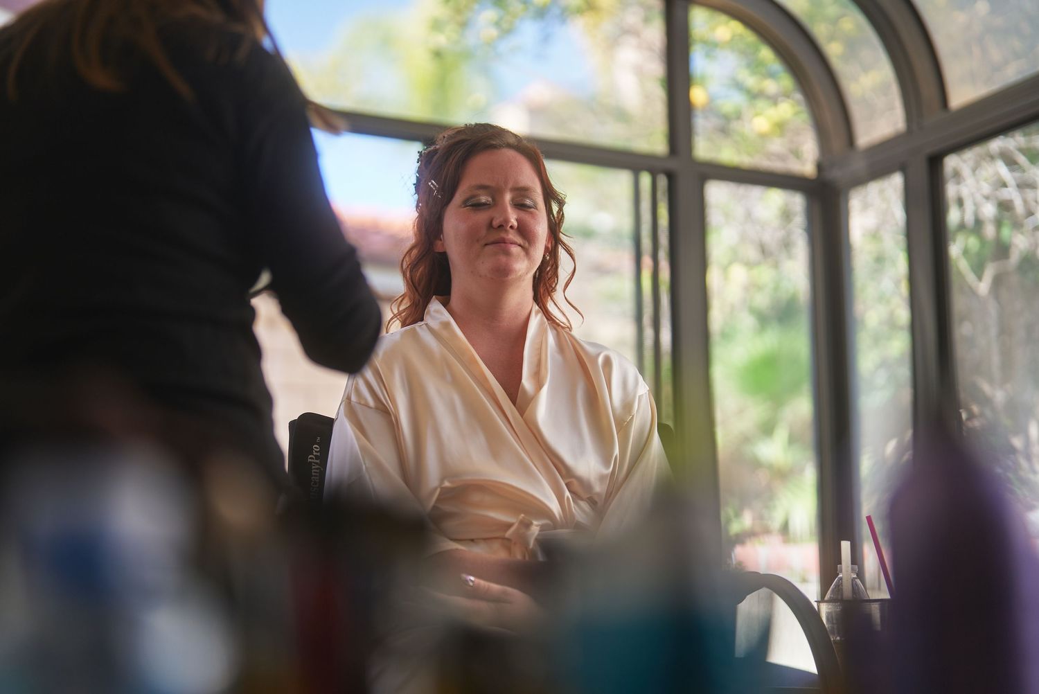Bride in white robe smiling during wedding hair and makeup preparation session indoors.