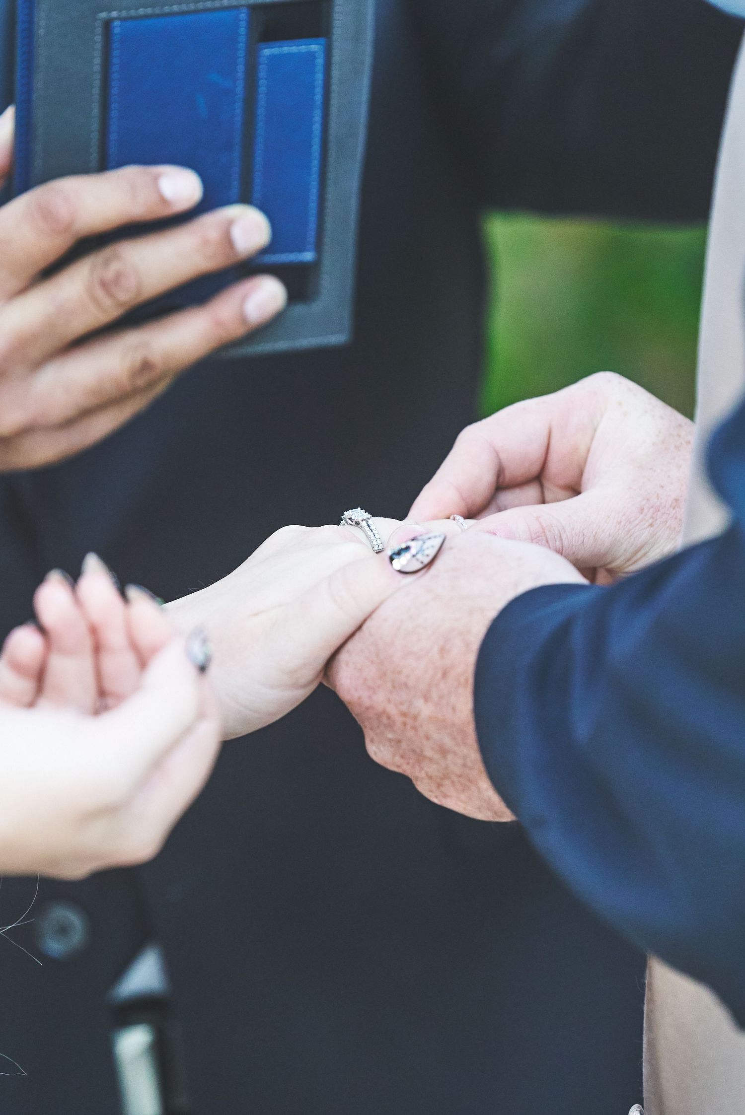 Close-up of a man placing a diamond engagement ring on a woman's finger during a proposal.