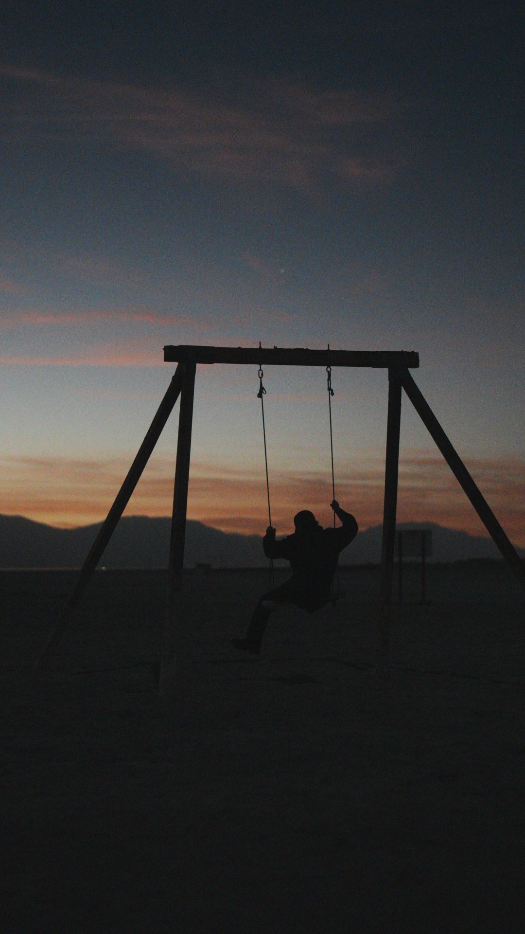 Silhouette of person on swing set against dramatic sunset sky.