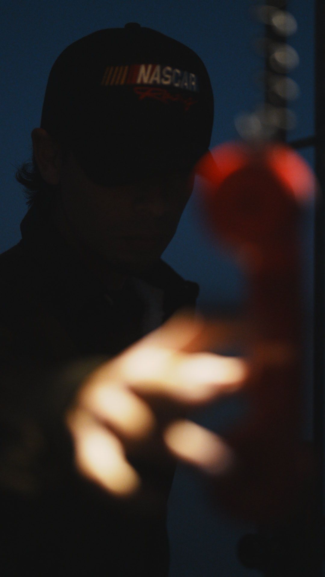 Silhouette of person wearing NASCAR cap in dark moody lighting.