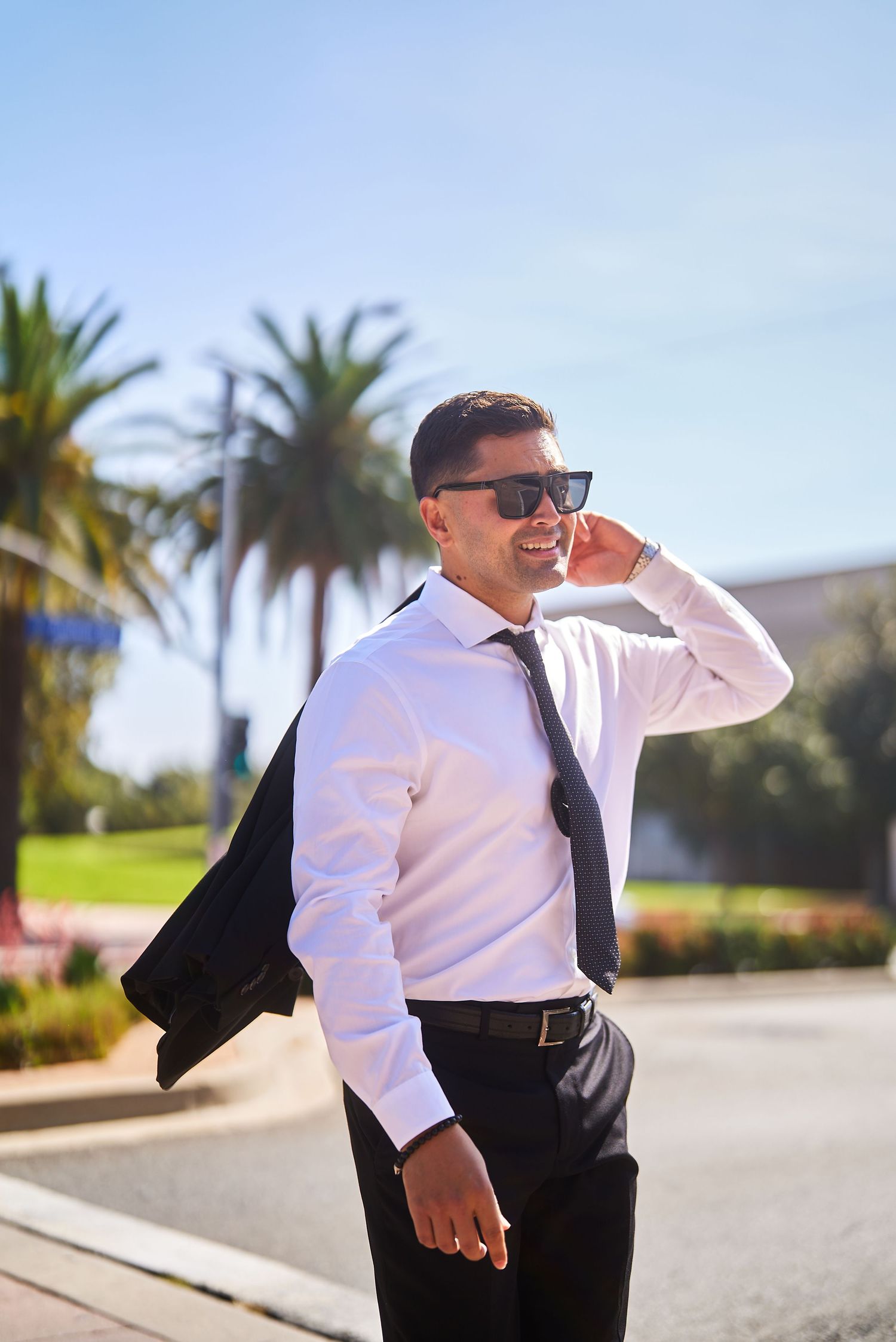 Professional in business attire talking on phone with palm trees in background.