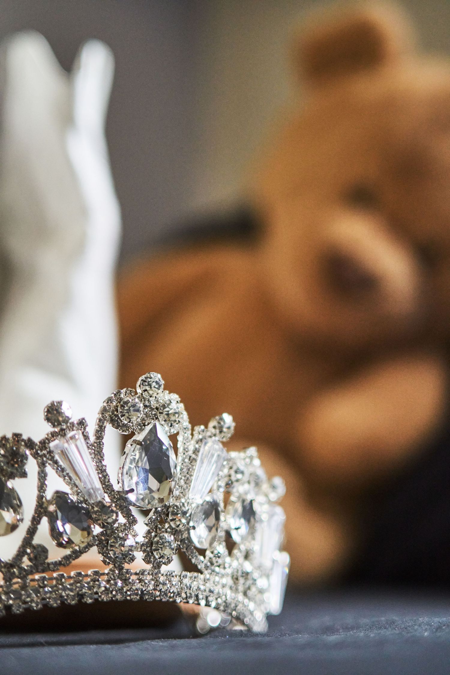 Ornate silver crystal crown with jewels photographed with soft focus teddy bear in background.