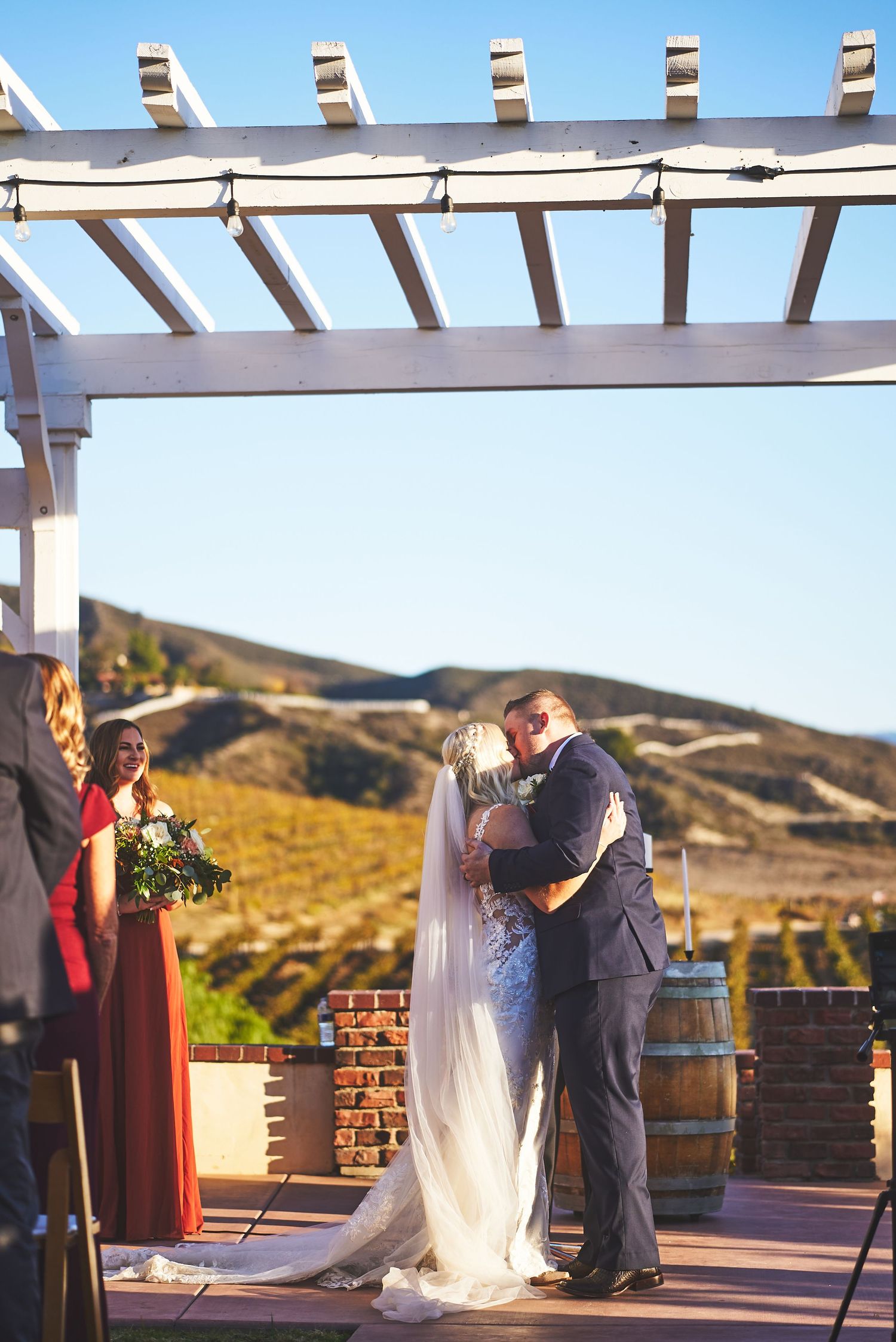 Outdoor wedding ceremony taking place under wooden pergola with mountain views.