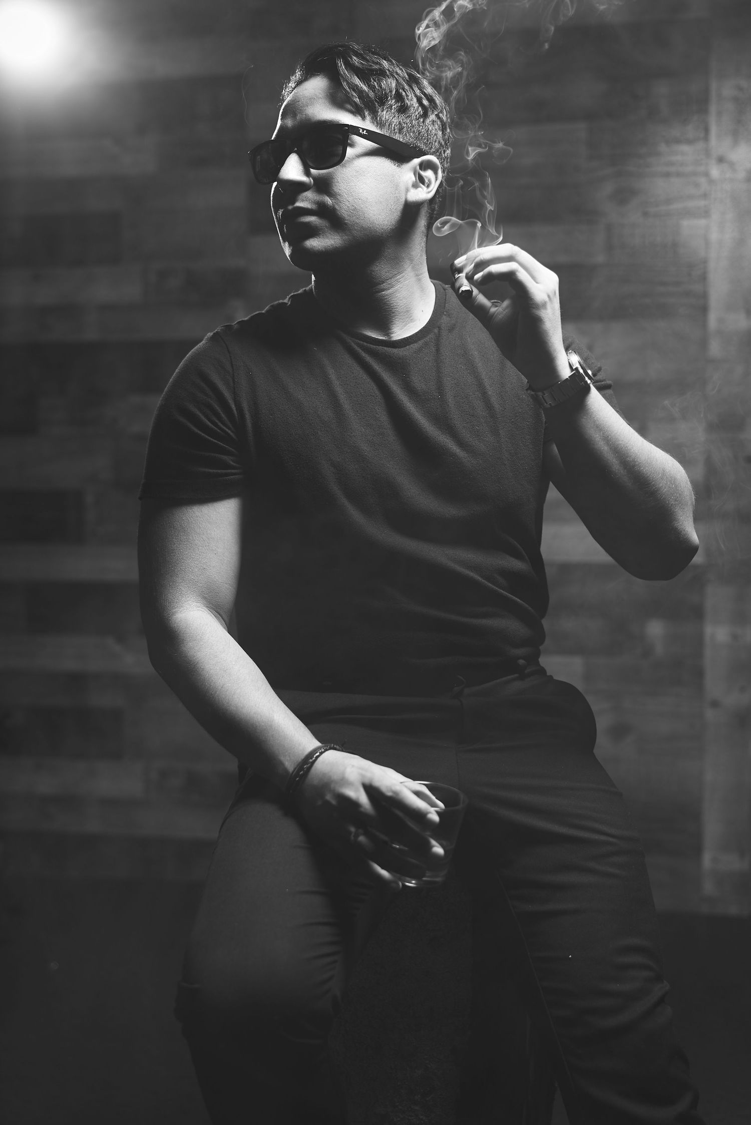 Moody black and white portrait of person in sunglasses smoking against dark background.