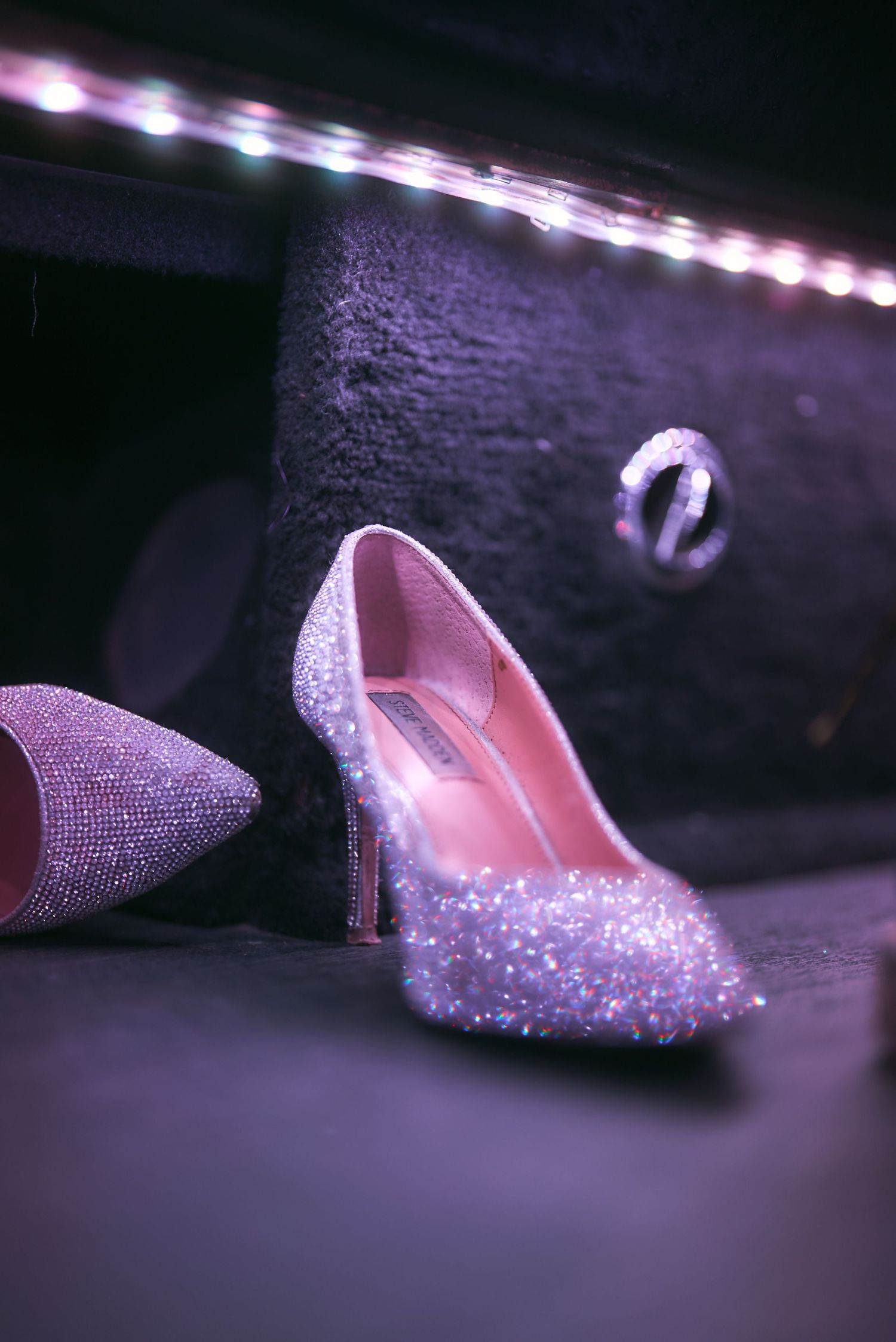 Close-up of sparkling crystal-encrusted high heel shoes under dramatic lighting.