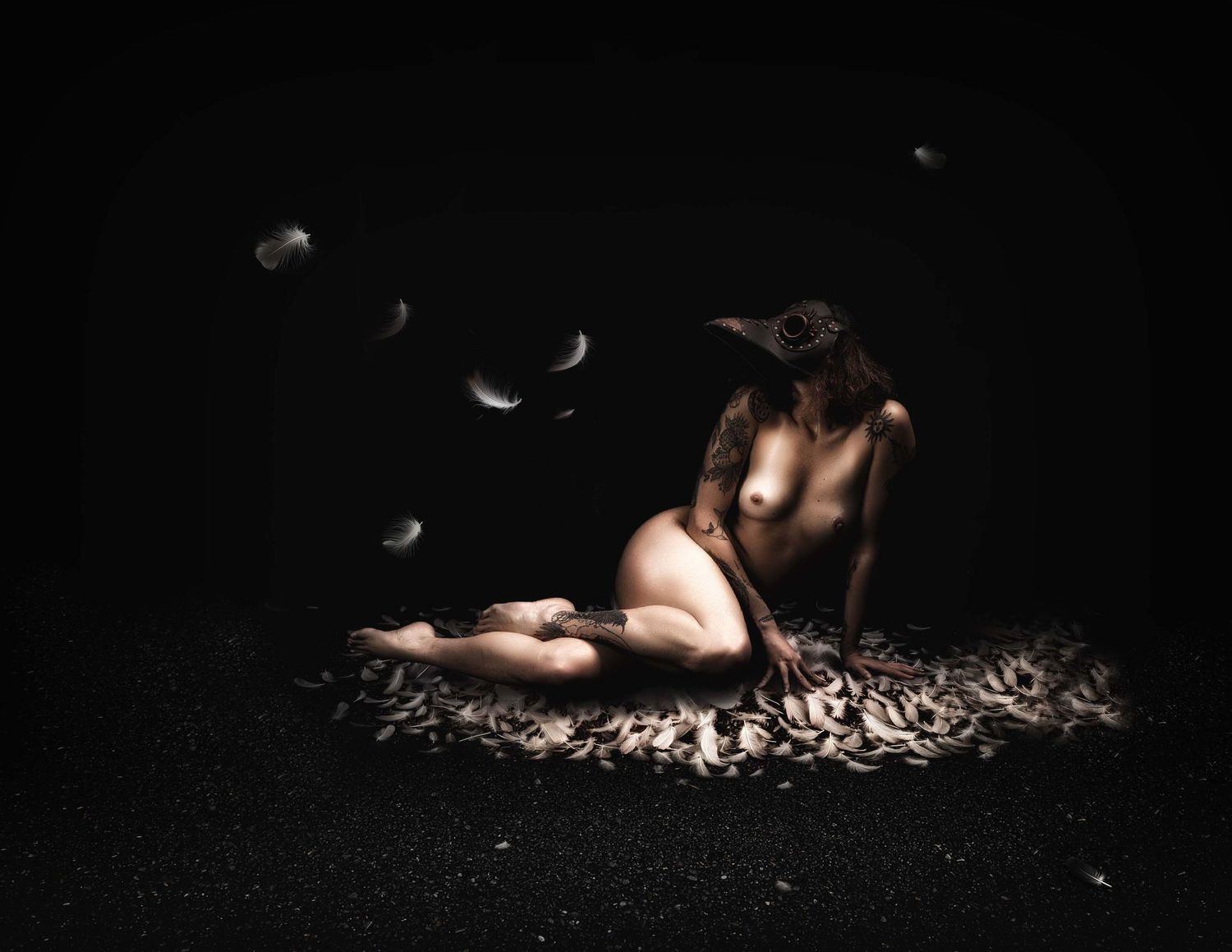 Surreal dark art of nude figure with bird mask sitting on feathers with floating feathers on black background.