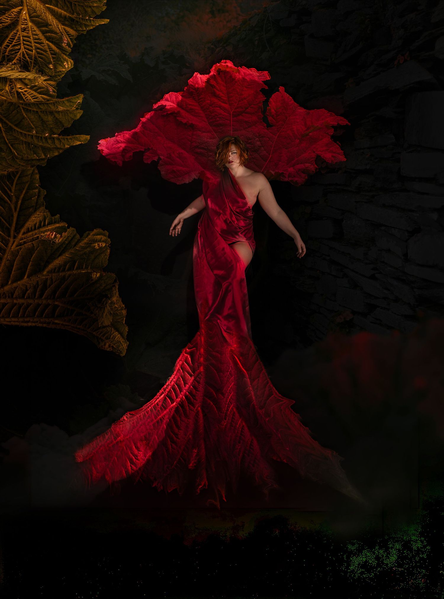 Woman in flowing red gown with dramatic petal-like cape floats ethereally against dark moody backdrop with golden leaves.