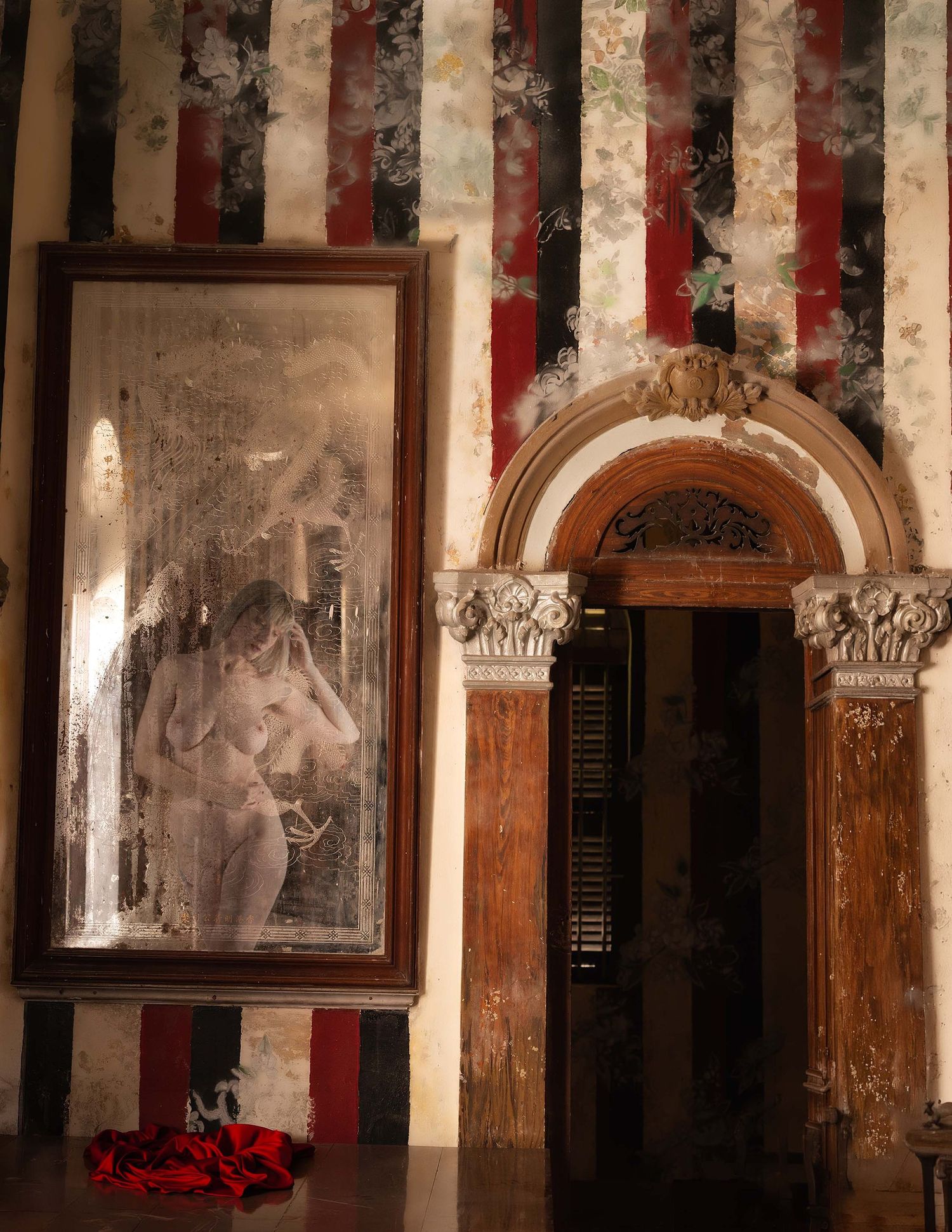 Ornate room with striped walls, a large framed nude painting, and an elegant arched wooden doorway.