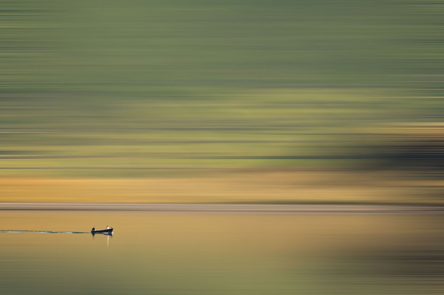 Silhouette of a small boat on calm water with soft green and golden horizontal motion blur reflections.