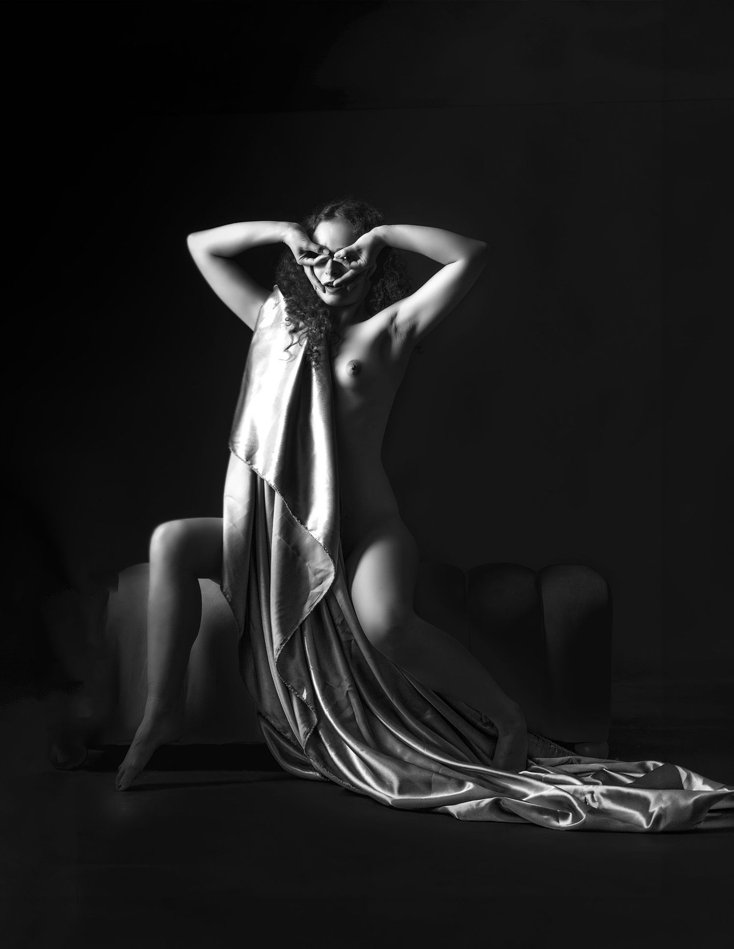 Black and white fine art nude photography of a woman draped in silk fabric, posed elegantly in dramatic studio lighting.
