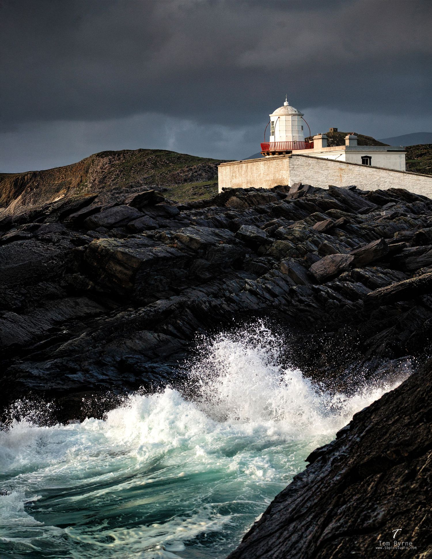 Dramatic lighthouse on rocky Irish coastline with crashing waves under stormy skies.