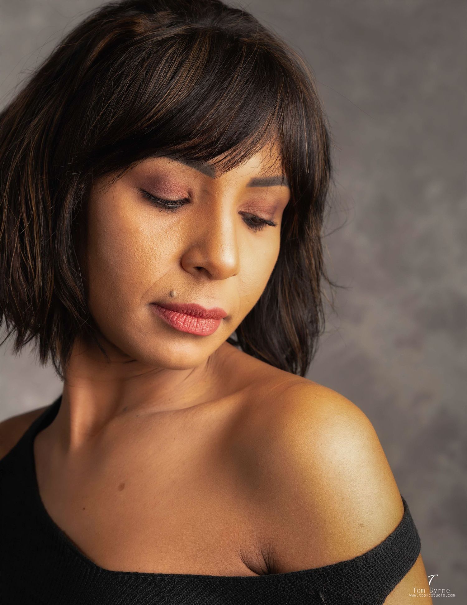 A woman with a short dark bob haircut poses gracefully with eyes downcast in a professional studio portrait.