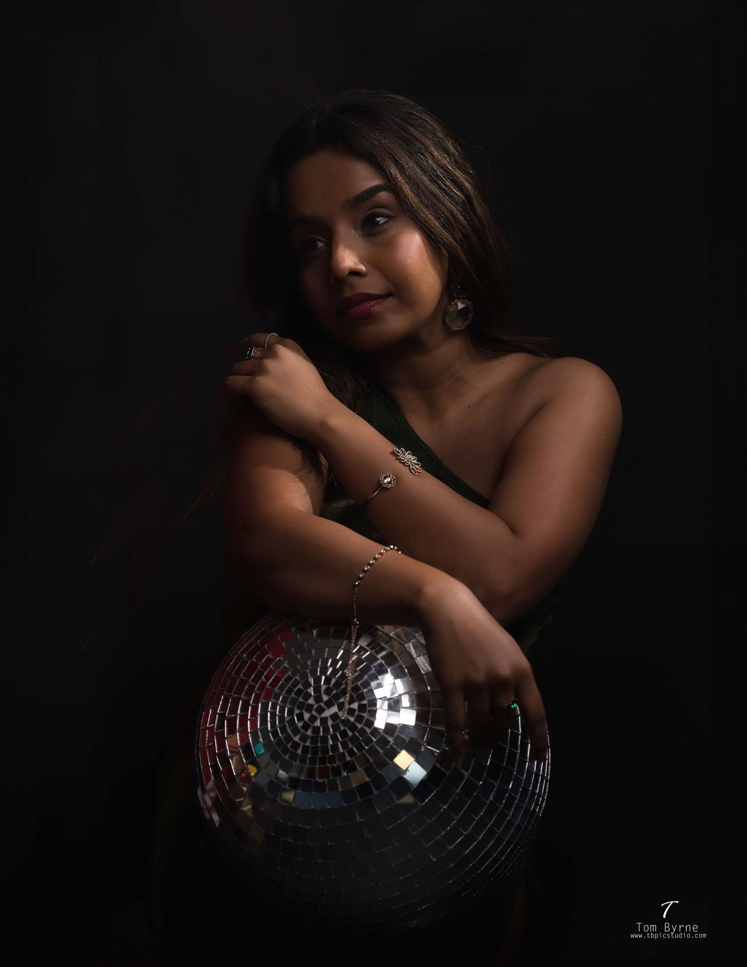 Young woman in elegant attire poses with a shiny disco ball against a dark background.