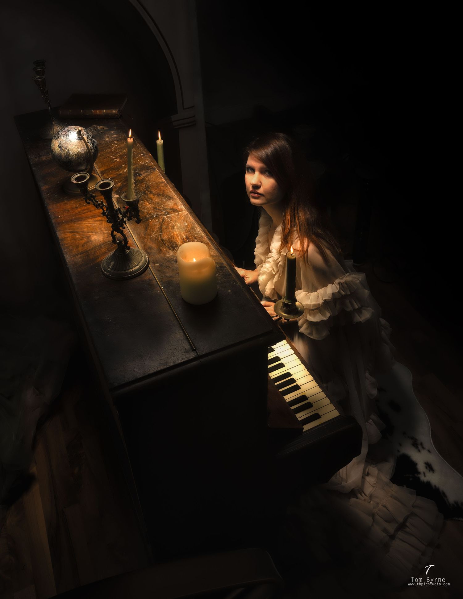 Young girl in white dress playing antique piano by candlelight in a dark, atmospheric setting.