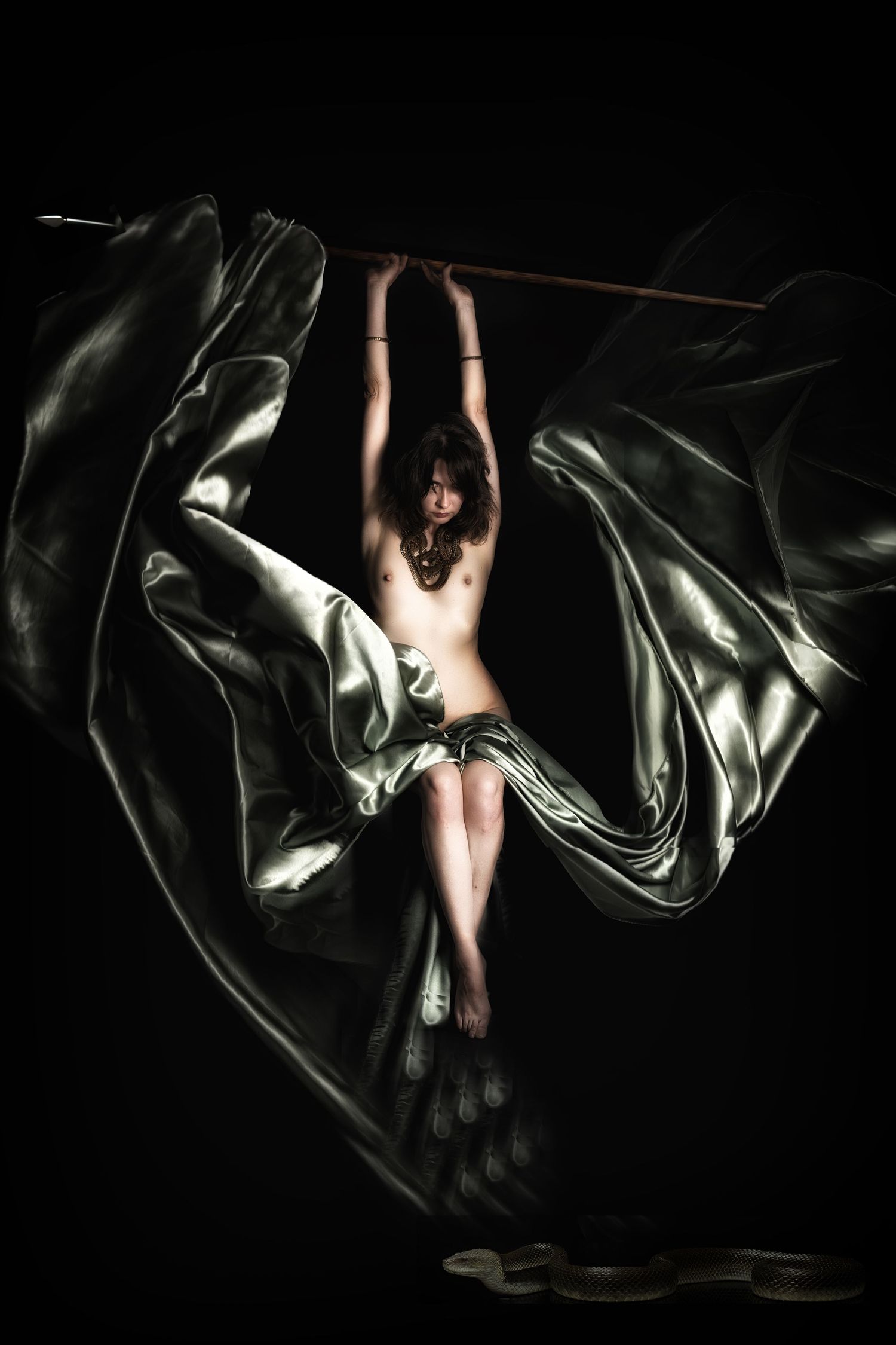 A dramatic fine art photo of a dancer suspended mid-air with flowing silver fabric against a dark background.