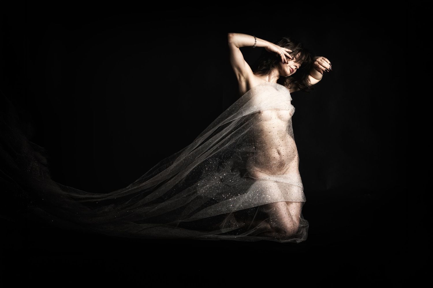 Artistic nude figure draped in flowing sheer fabric against dark background, elegant dance pose.