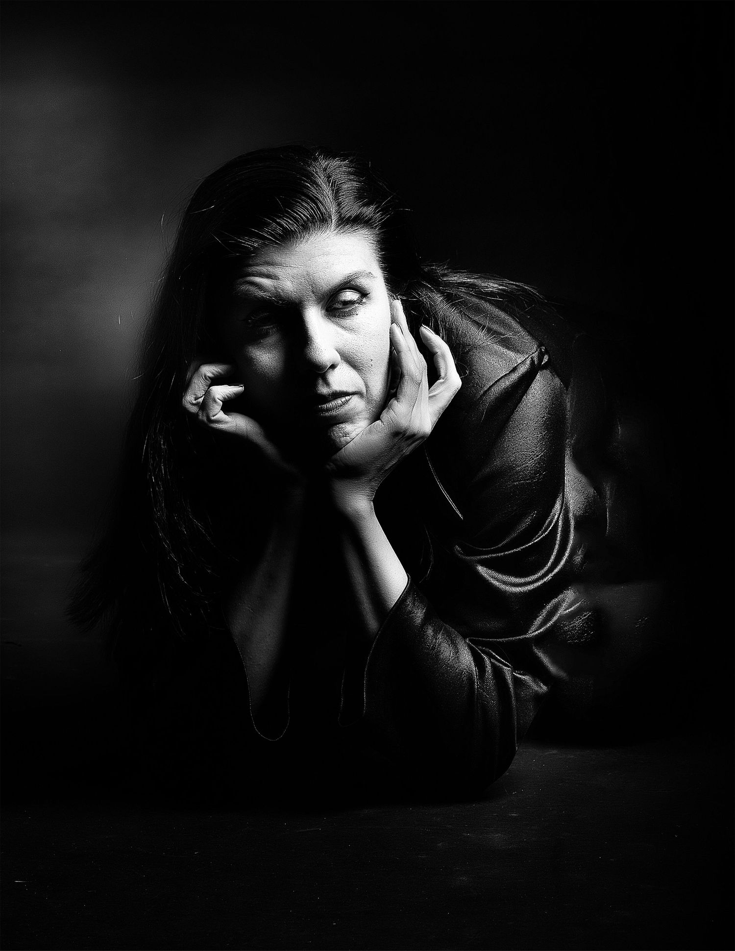 Black and white portrait of a woman resting her chin on her hands, dramatic studio lighting.