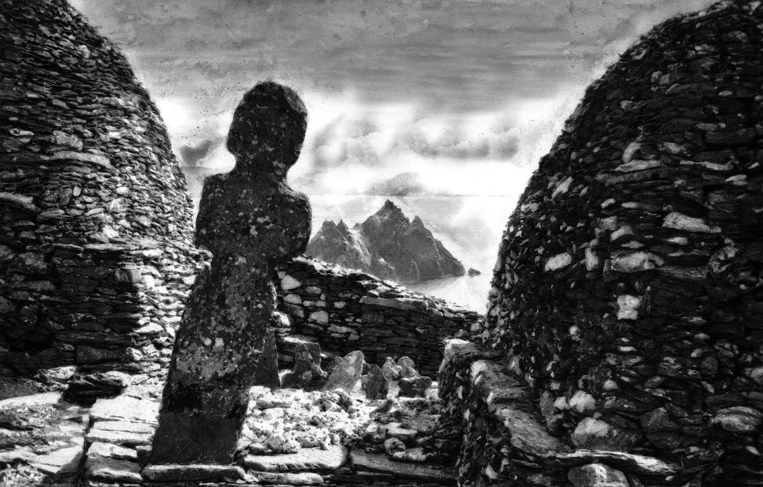 Black and white photo of ancient stone beehive huts at Skellig Michael, Ireland, with dramatic rocky peaks in background.