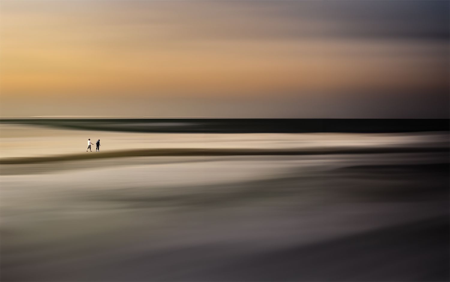 Two silhouetted figures stand on a serene beach at sunset with soft blurred waves and a glowing horizon.