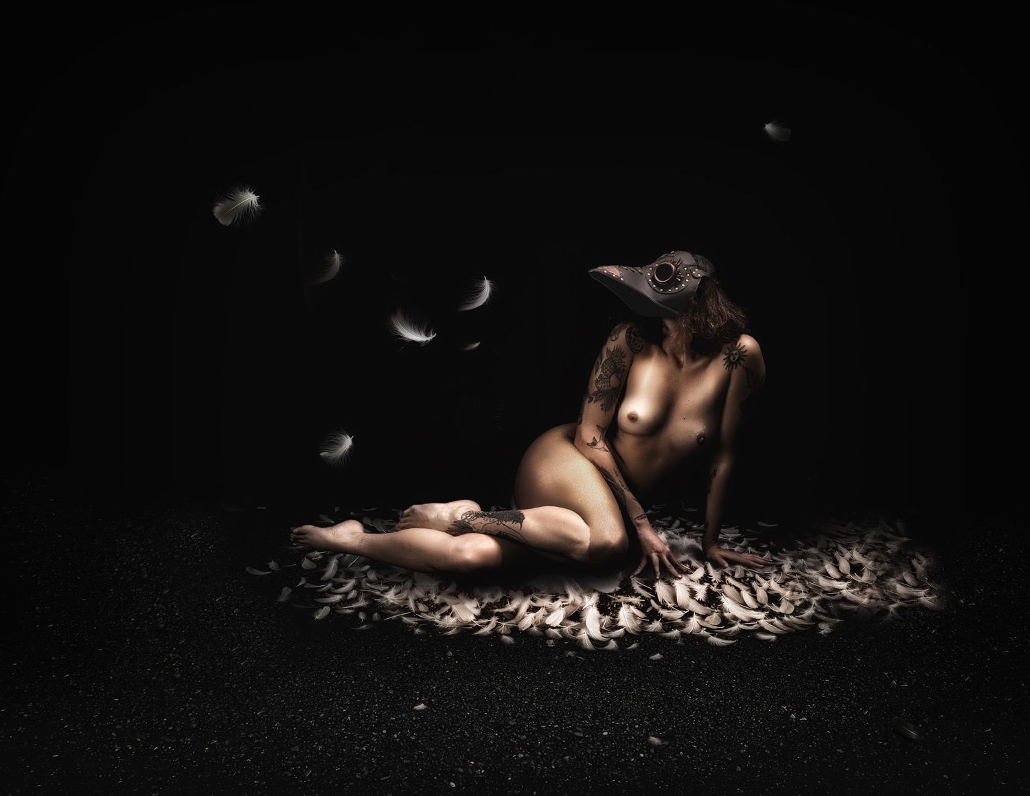 A nude figure wearing a bird mask reclines on feathers in dramatic dark lighting with floating feathers above.