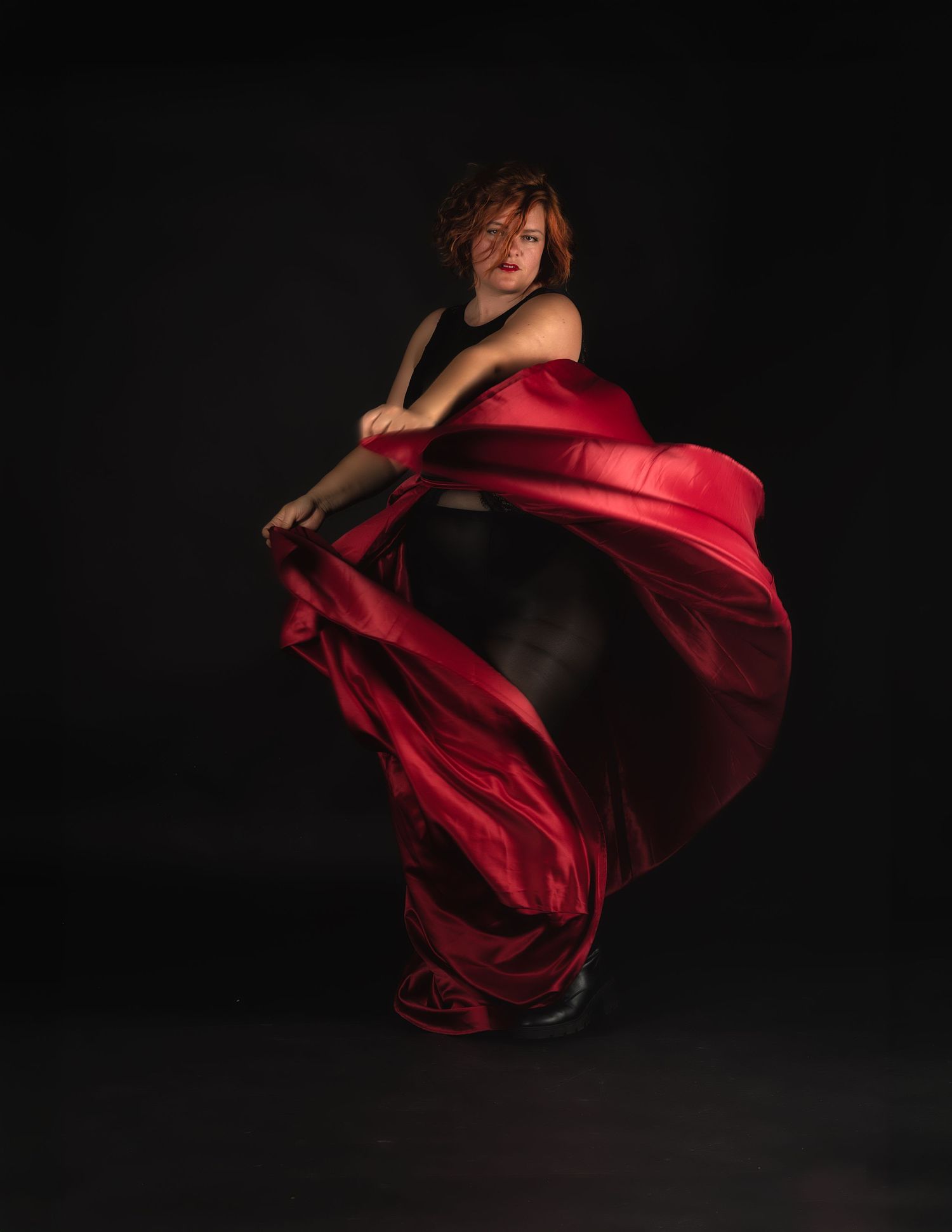A dancer in a black outfit twirls a flowing red silk fabric against a dark background.