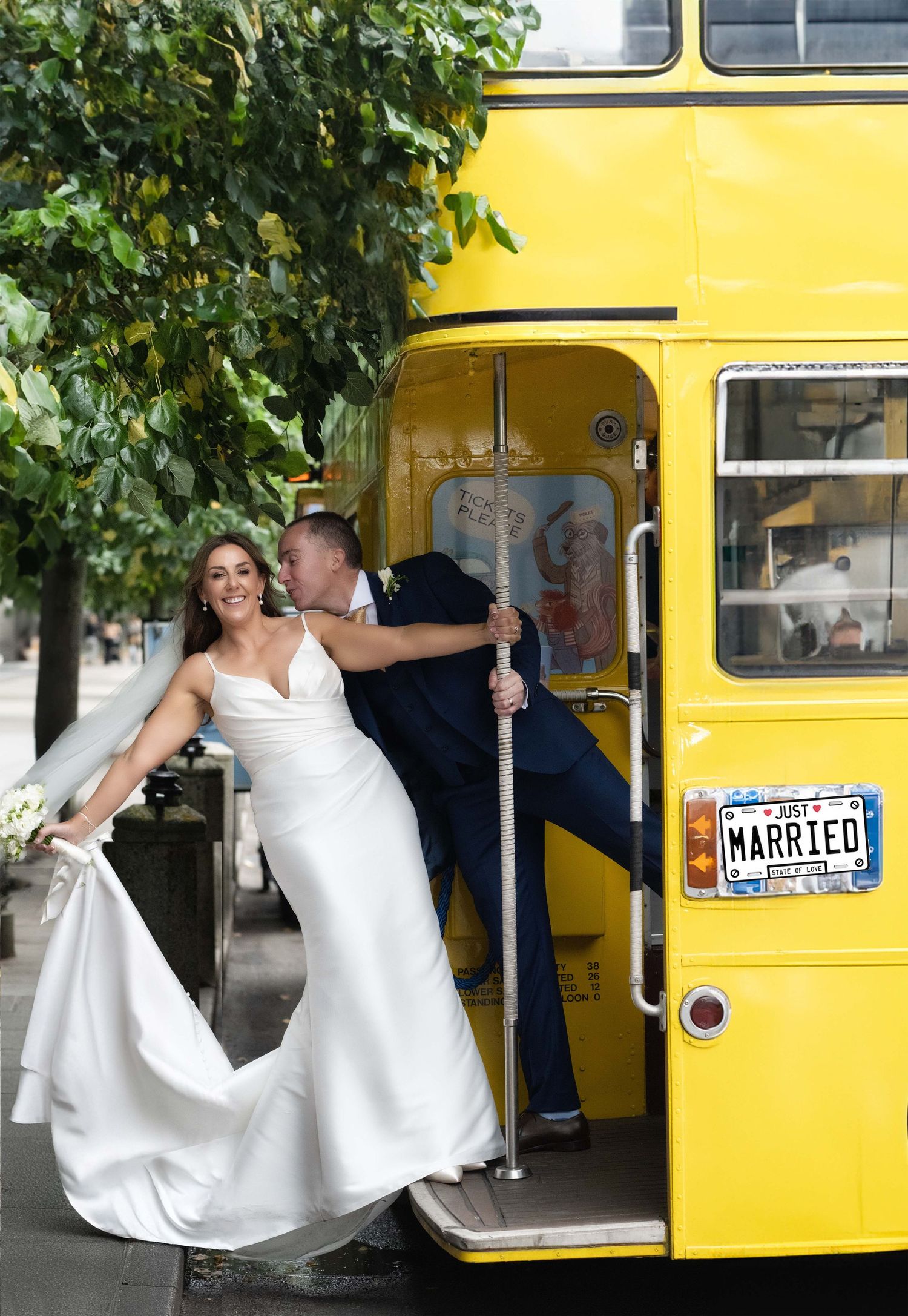 Bride and groom posing on a yellow double-decker bus with a MARRIED license plate on their wedding day.