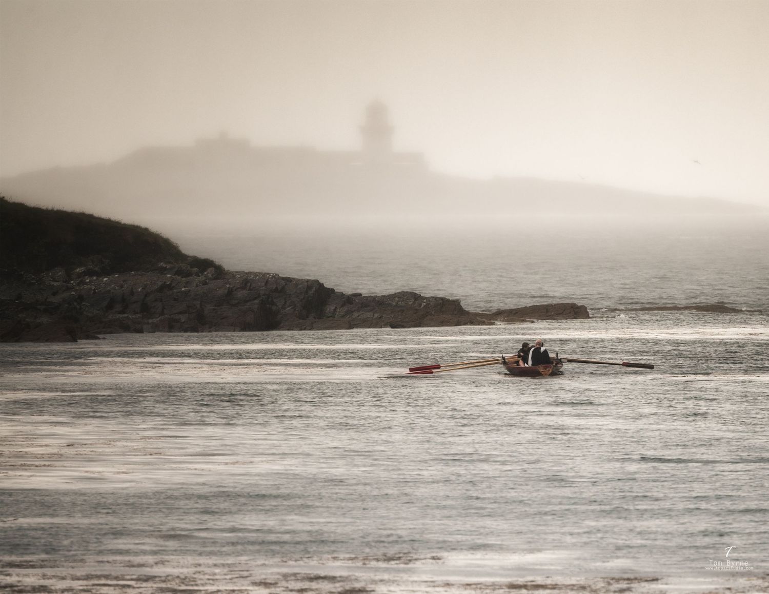 Rowers navigate misty coastal waters with a lighthouse silhouetted on rocky cliffs in the foggy background.