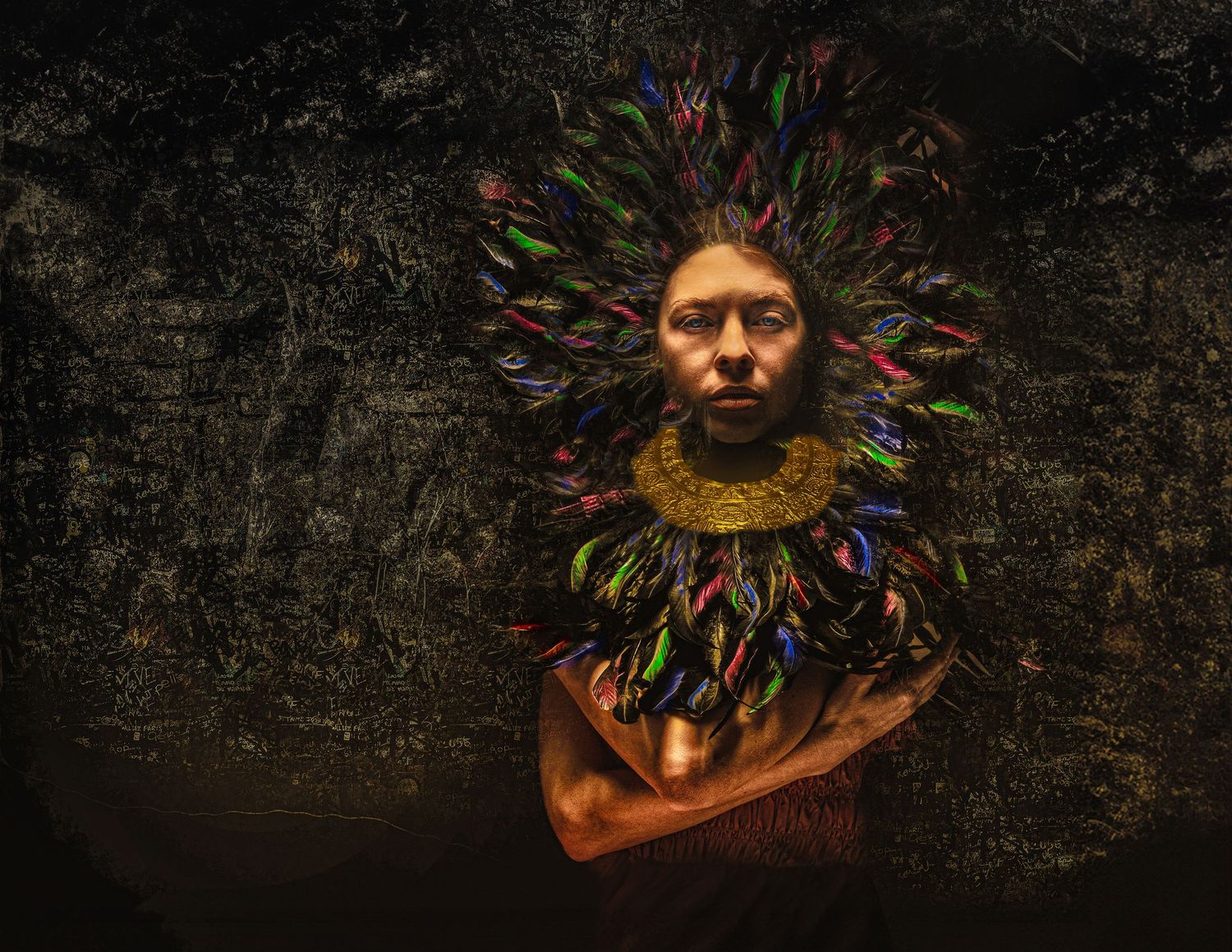 Person wearing colorful feathered headdress and necklace against dark textured background in dramatic artistic portrait.