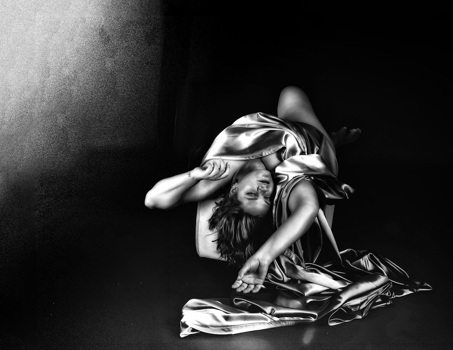 Black and white photo of a dancer draped in silk fabric, curled on the floor in an expressive, dramatic pose.