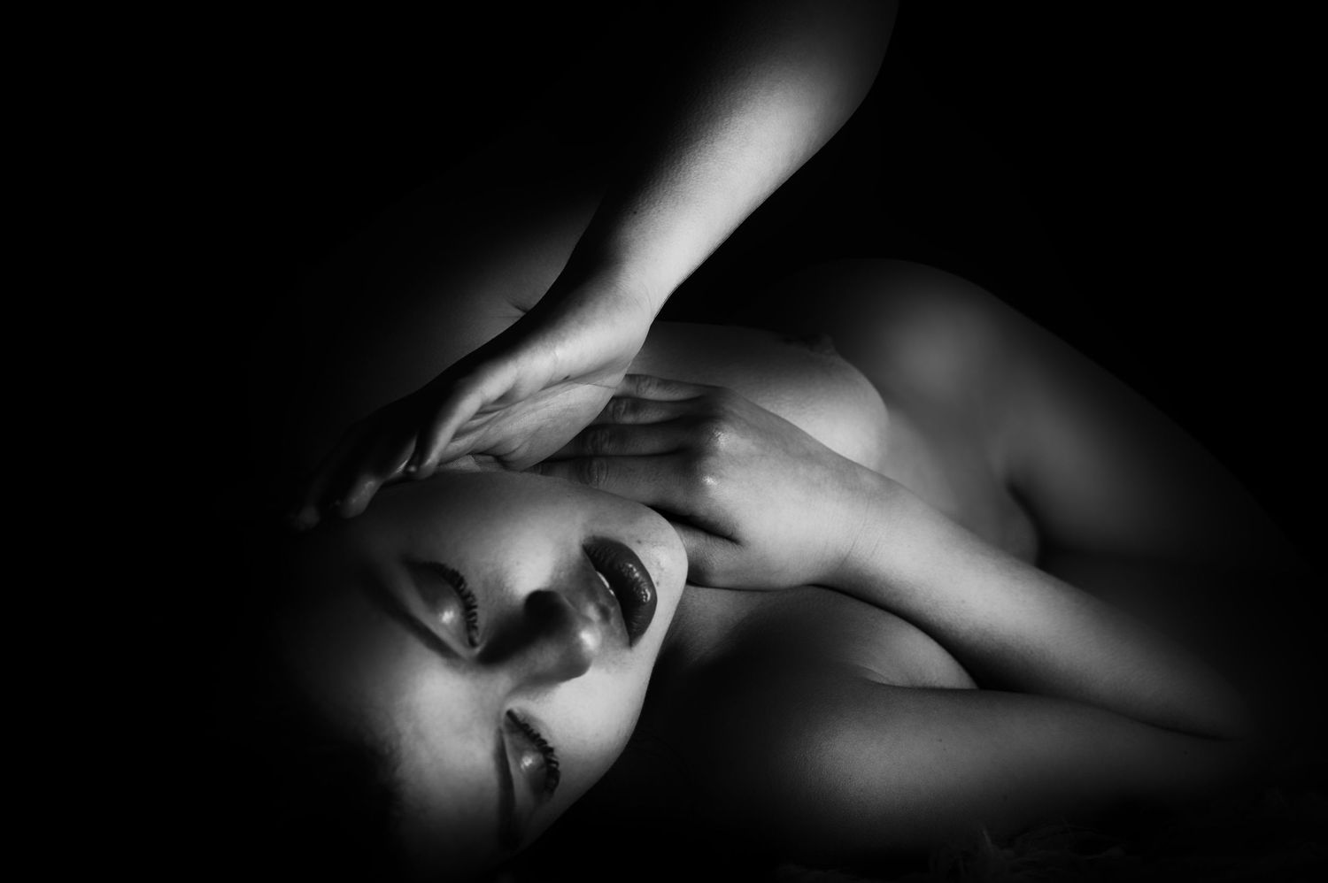 Black and white artistic portrait of a woman lying down with dramatic lighting and shadows.