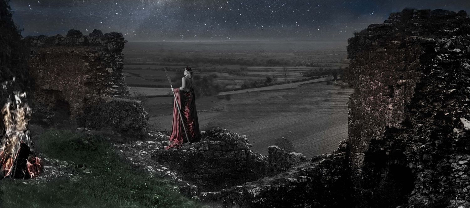 A mysterious robed figure stands atop ancient ruins under a starry night sky overlooking a vast dark landscape.
