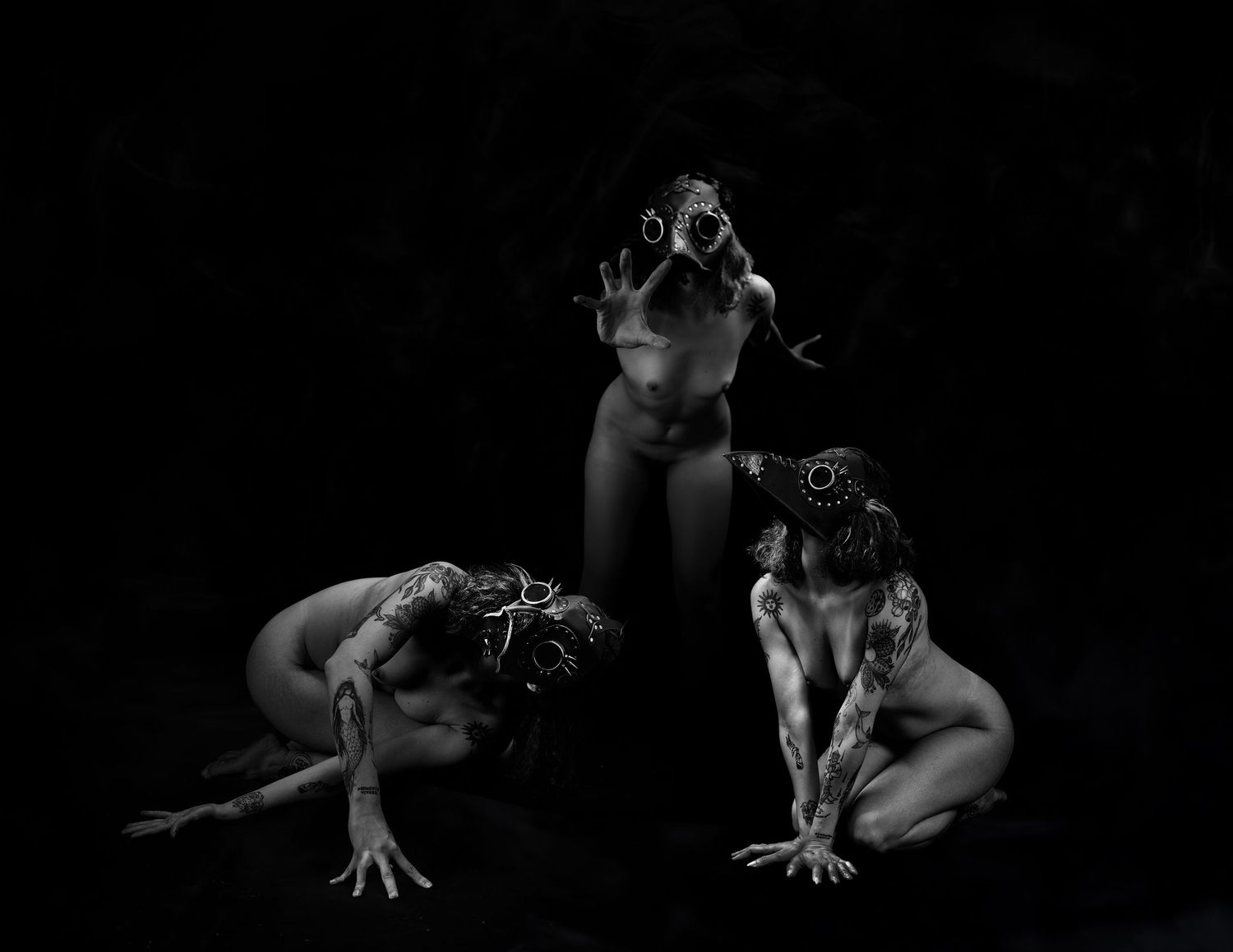 Three figures in dramatic black and white fine art photography wearing bird masks in dark atmospheric studio setting.