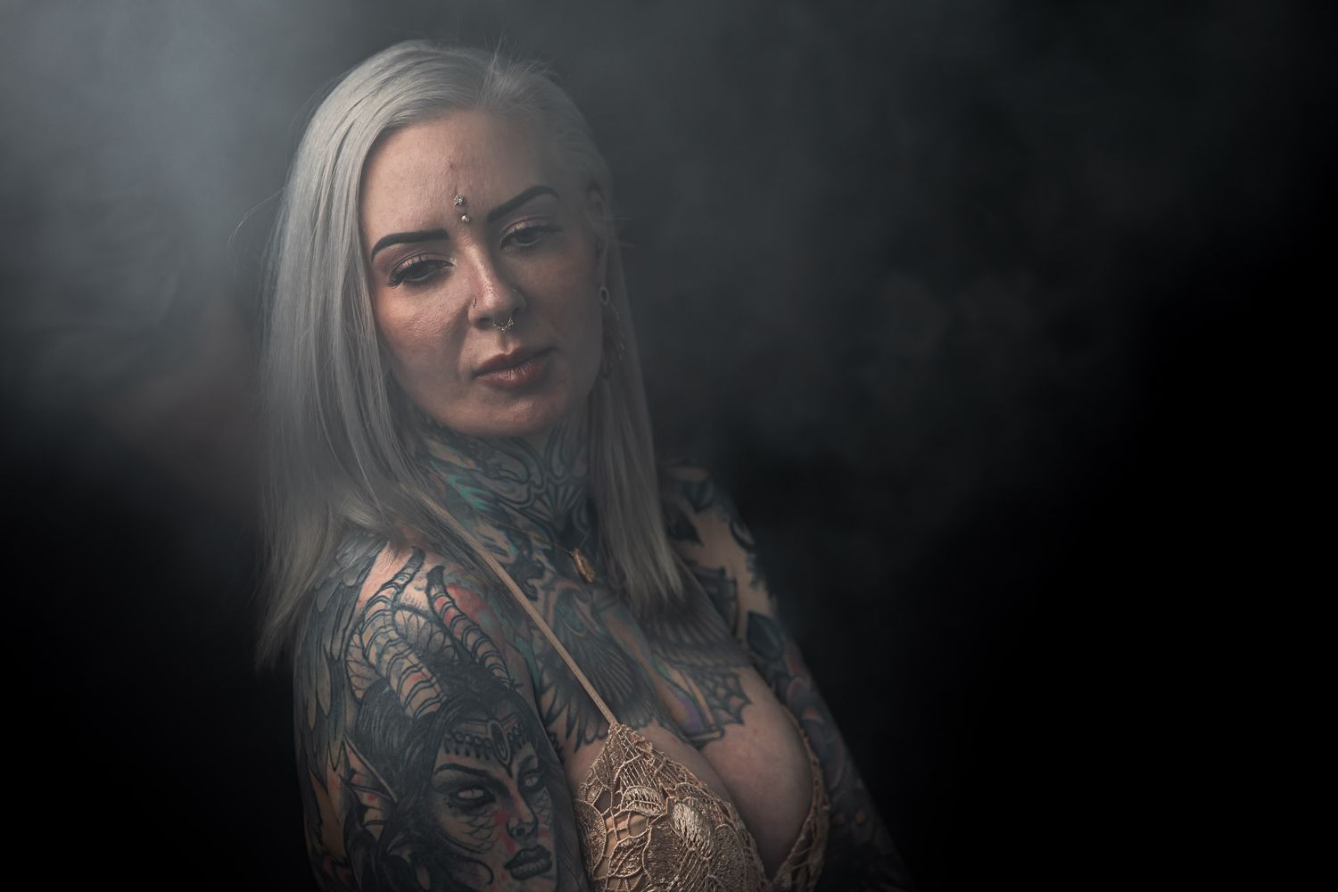 Tattooed woman in lace top portrait with soft dramatic lighting and dark background, fine art studio photography at Unique Photo event