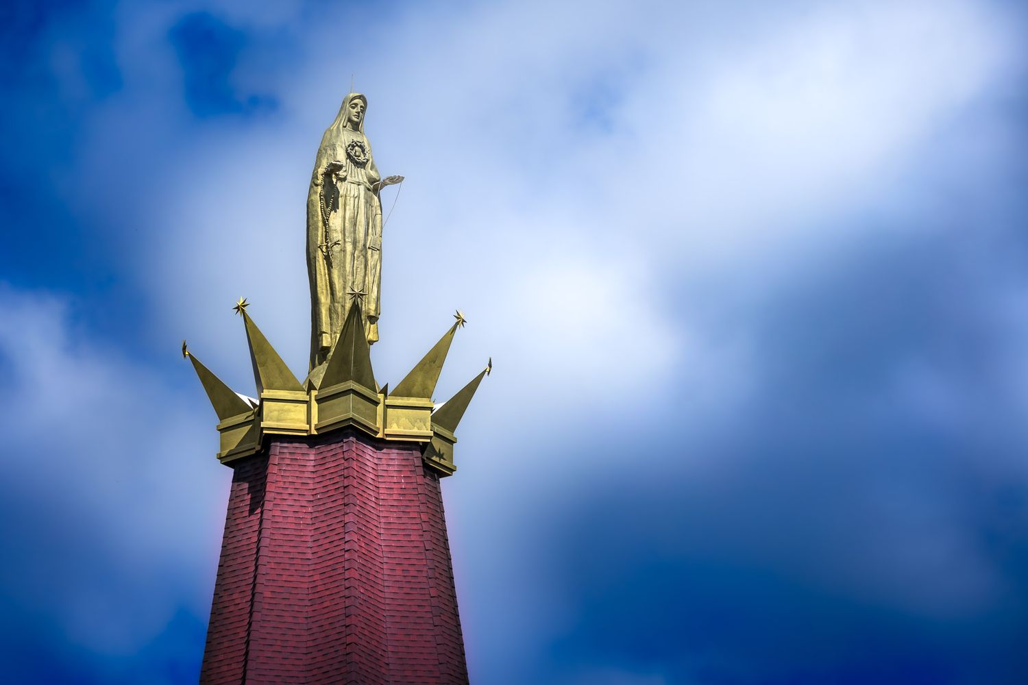 Golden statue atop the National Blue Army Shrine of Our Lady of Fatima in Washington, New Jersey, photographed against a blue sky