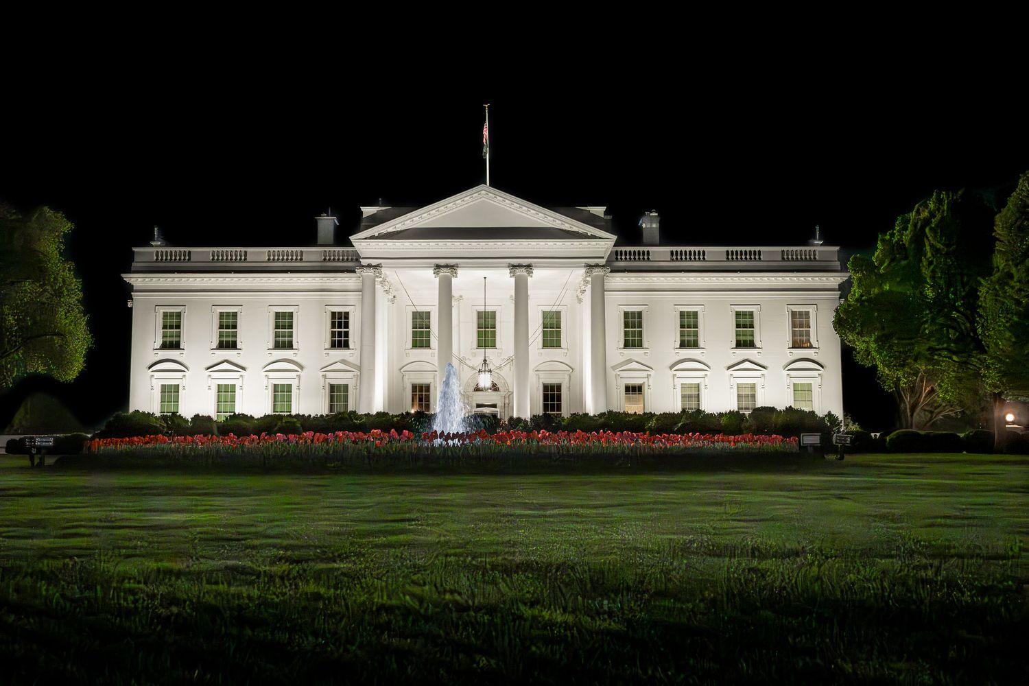 The White House at night in Washington DC, illuminated against a dark sky, photographed through the fence with long exposure.