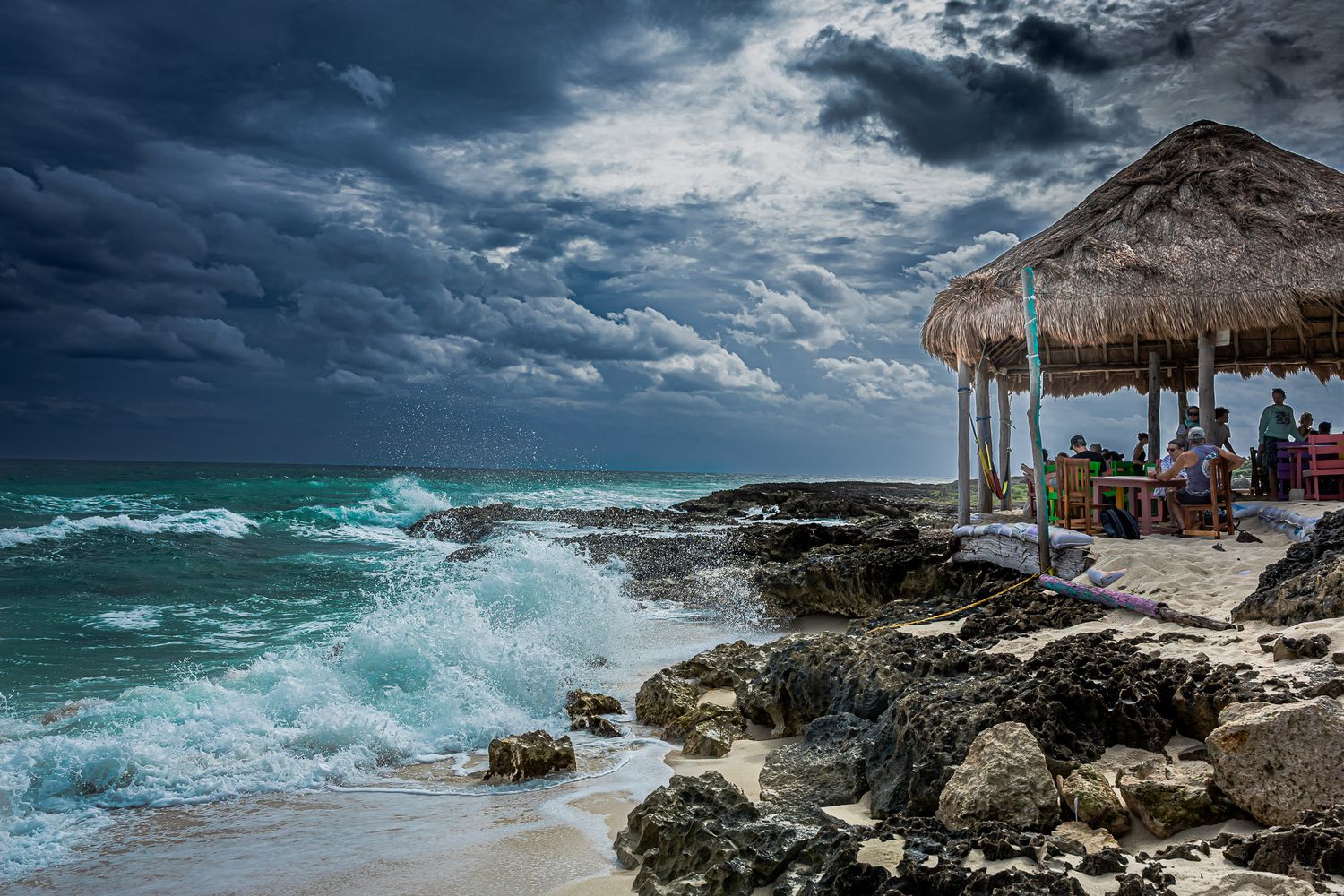 Ocean waves crashing against rocky shore near a beach side restaurant in Cozumel, Mexico under dramatic storm clouds