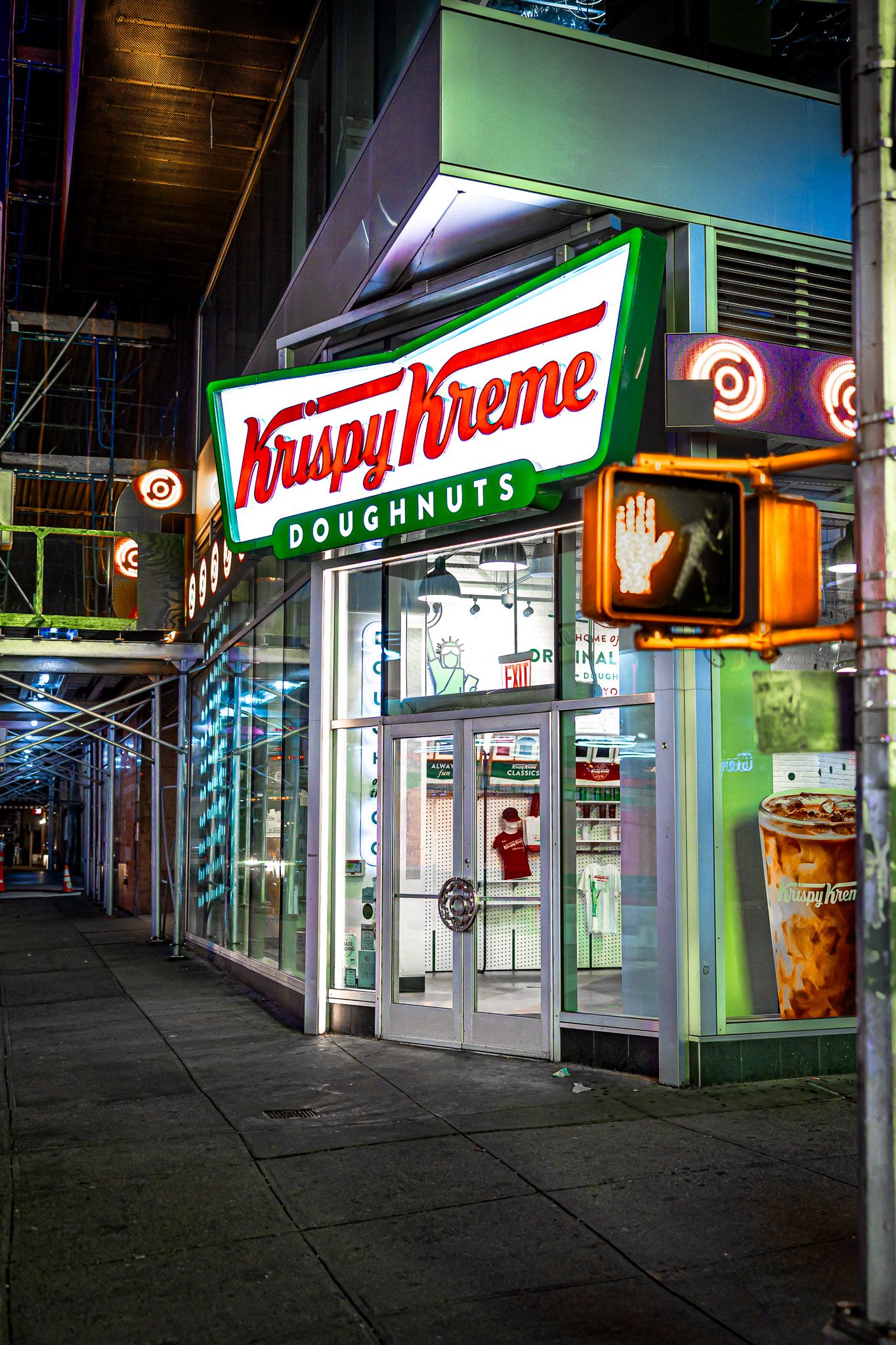 Krispy Kreme storefront illuminated at night with a pedestrian stop signal in Times Square, New York City.