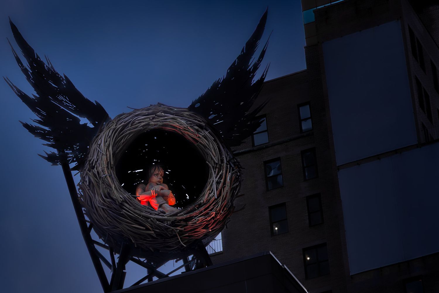 Illuminated winged nest sculpture atop a Broadway theater in Times Square at dusk, New York City.