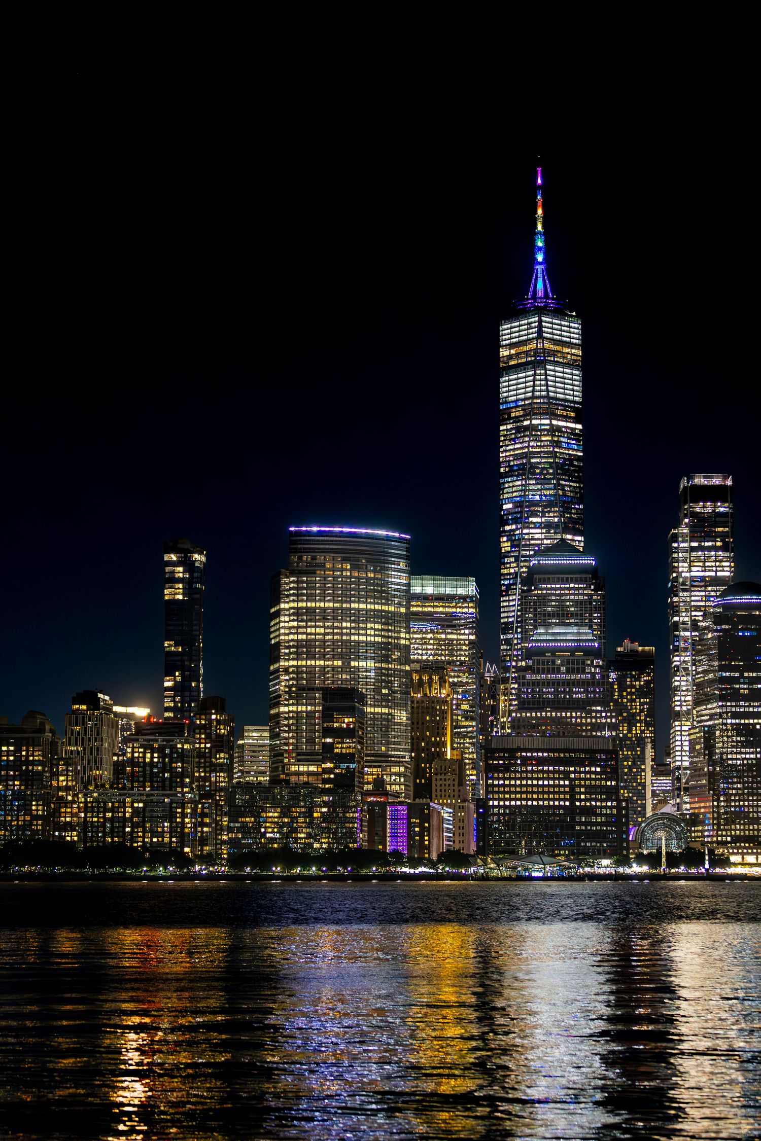 New York City skyline at night with One World Trade Center illuminated, viewed across the Hudson River from Jersey City, New Jersey.