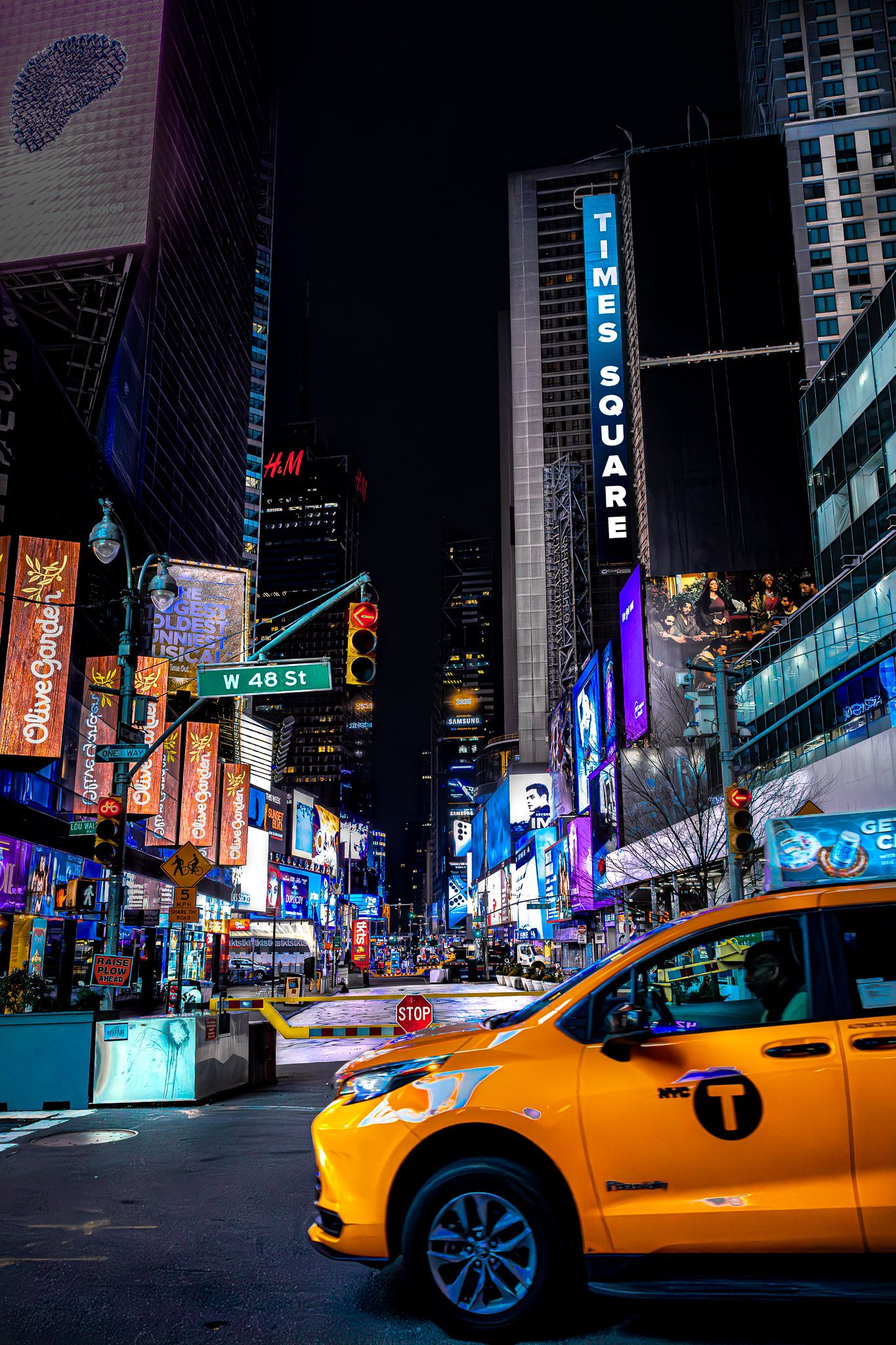Yellow taxi driving through Times Square at night surrounded by bright billboards and city lights in New York City.