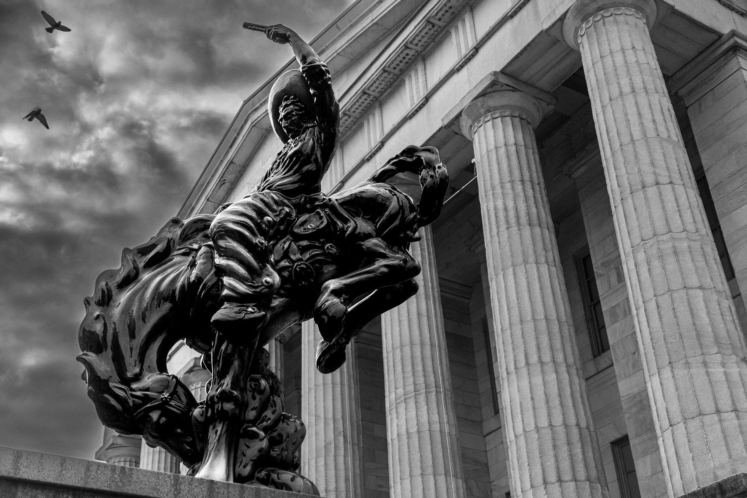 Black & white photograph of an equestrian statue at the National Portrait Gallery in Washington DC with dramatic clouds and birds in flight