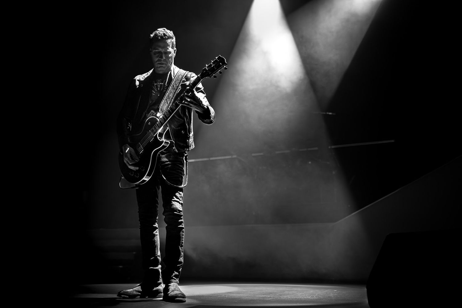 Black and white photograph of a guitarist performing on stage under dramatic concert lighting.