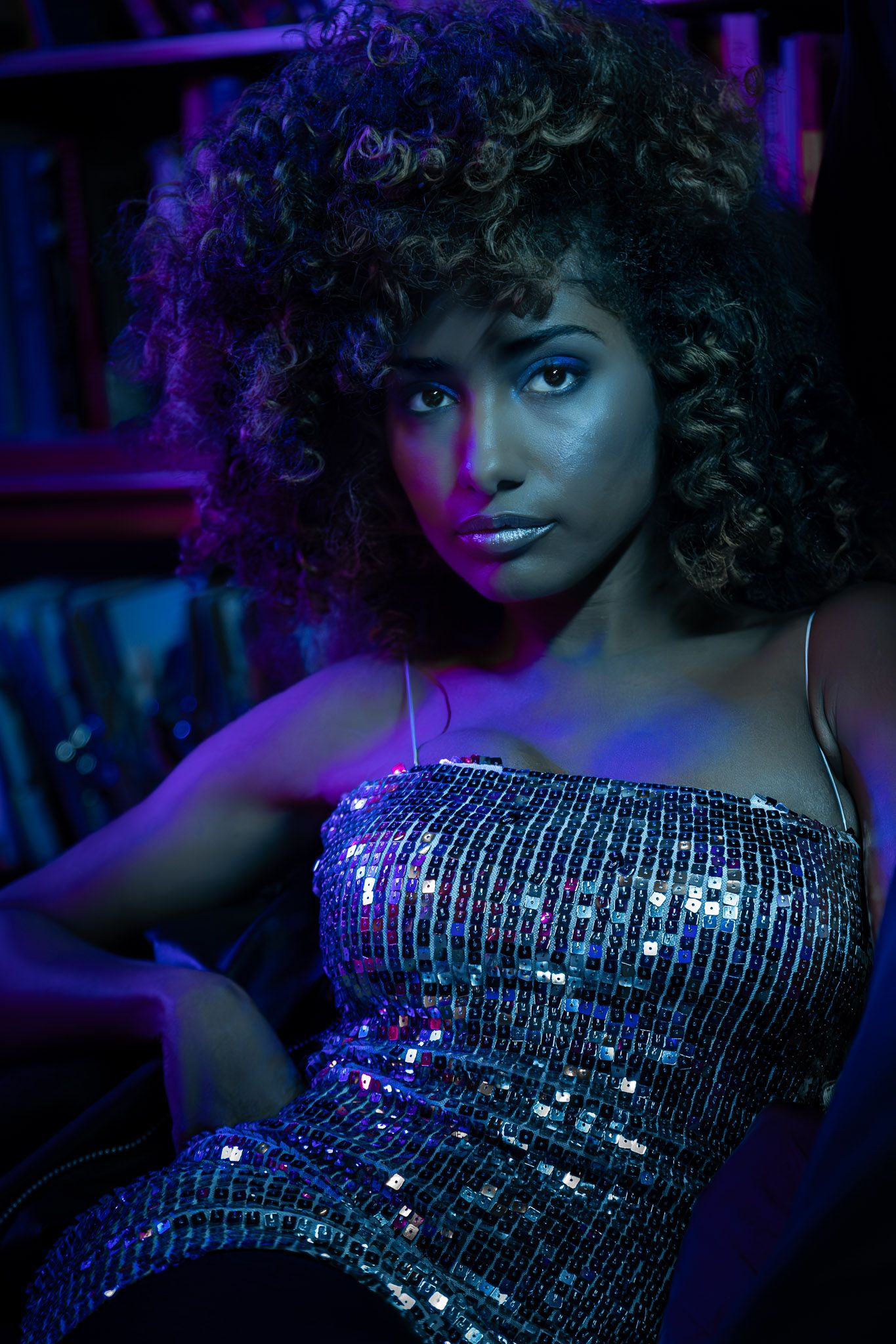 Moody studio portrait of a woman in a sequined dress lit with blue and purple cinematic lighting during a Unique Photo photography event in