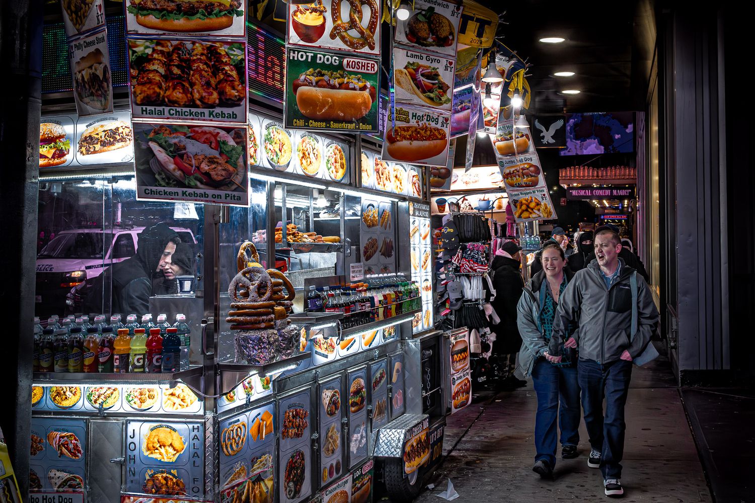 Late-night Times Square street scene with crowded food cart, glowing menus, and pedestrians moving through the city.
