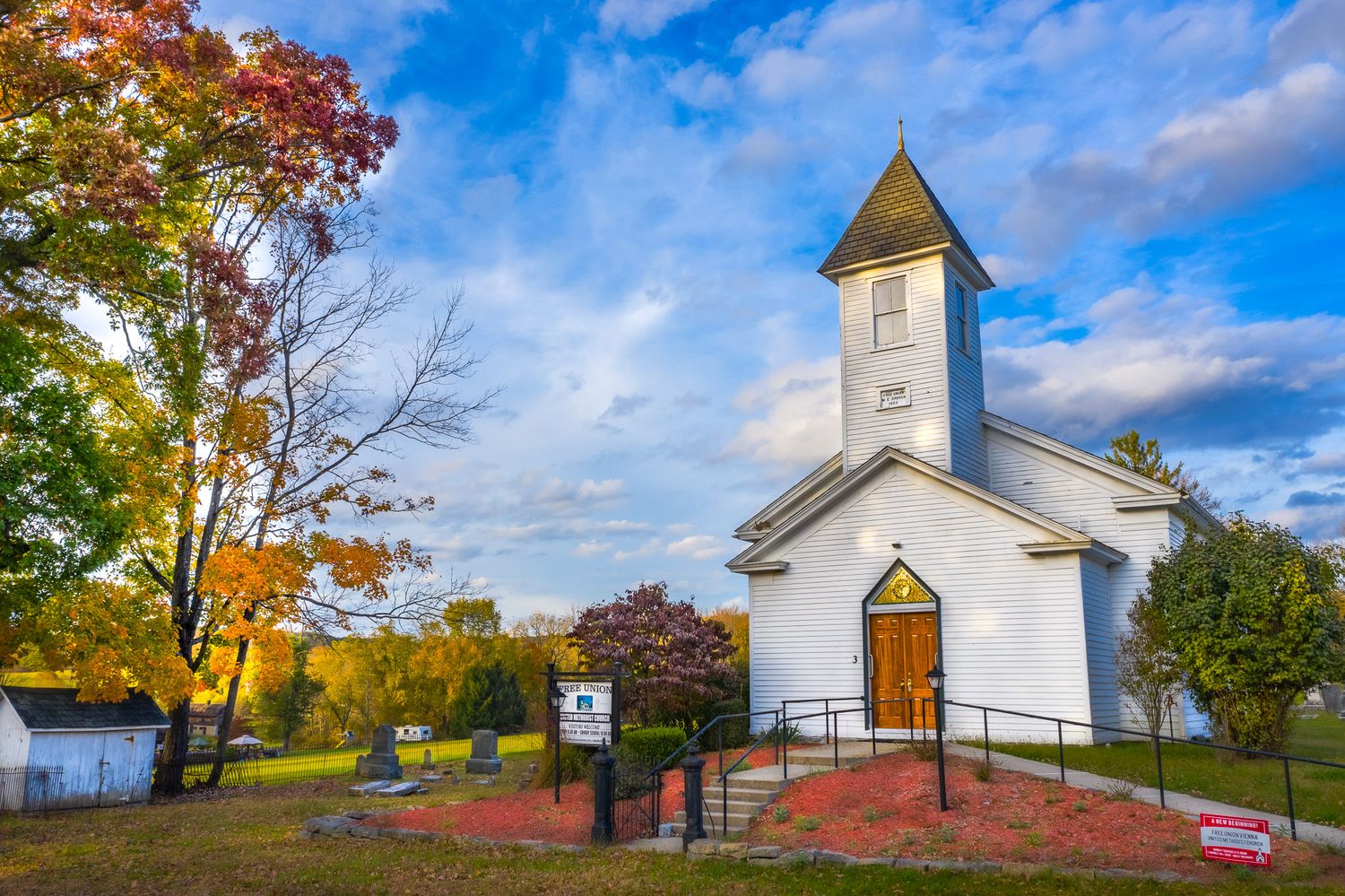 Historic Free Union United Methodist Church in Great Meadows, NJ photographed in fall with colorful trees and blue sky.